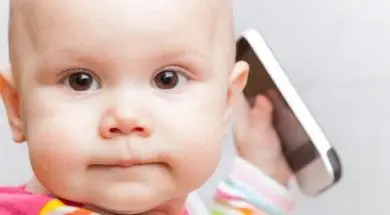 Little baby in casual colorful striped clothing plays with mobile phone