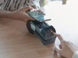 Woman paying bill through smartphone using NFC technology in a coffee. customer paying through mobile phone using contactless technology. Closeup hands of mobile payment at a coffee shop