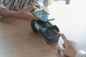Woman paying bill through smartphone using NFC technology in a coffee. customer paying through mobile phone using contactless technology. Closeup hands of mobile payment at a coffee shop